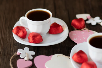 Fototapeta na wymiar Valentine's Day concept. Two white cups of coffee and heart-shaped sweets on a brown wooden background.