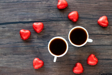 Chocolate candies in a red wrapper and two cup of coffee on a brown wooden background. Top view.