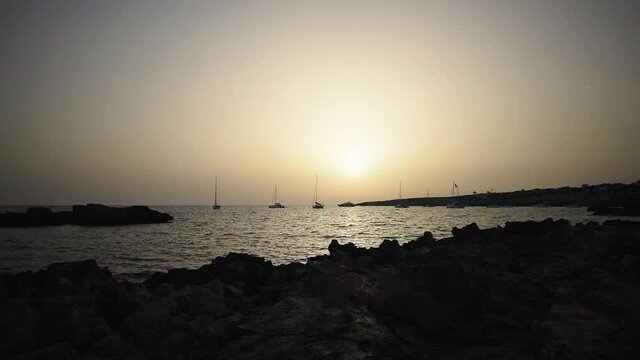 Sunrise on a rocky beach of the island of Formentera with boats anchored in the bay. Real-time HD quality video