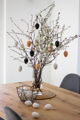 Fresh flowering branches decorated with easter colorful eggs in a vase on a wooden table.