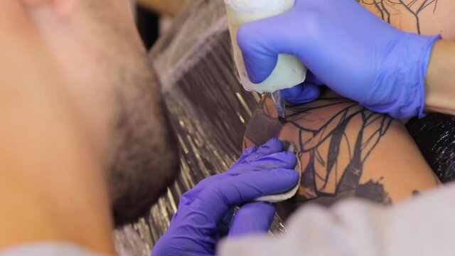 Tattoo artist make a black tattoo on man's skin with a tattoo machine. Close up