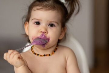 Cute little baby girl eating purple blueberry yogurt with spoon.