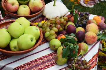Apples, pears, plums, grapes, peaches, pumpkin and watermelon on an embroidered towel and in a clay dish with an ornament, background
