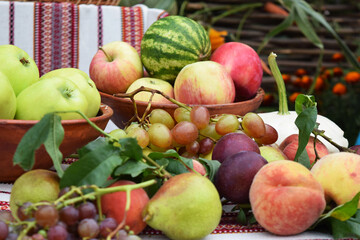 Apples, pears, plums, grapes, peaches, pumpkin and watermelon on an embroidered towel and in a clay dish with an ornament, background