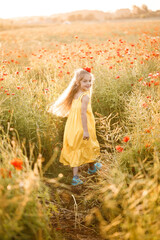 Fototapeta na wymiar Little girl in a yellow dress runs in red poppy flowers on a background of green grass