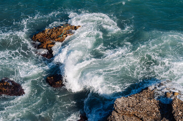 Aerial drone view of the ocean and waves crashing on rocks.