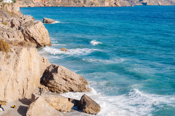 Aerial top view of sea waves hitting rocks on the beach with turquoise sea water. 