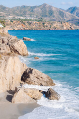 Aerial top view of sea waves hitting rocks on the beach with turquoise sea water. 