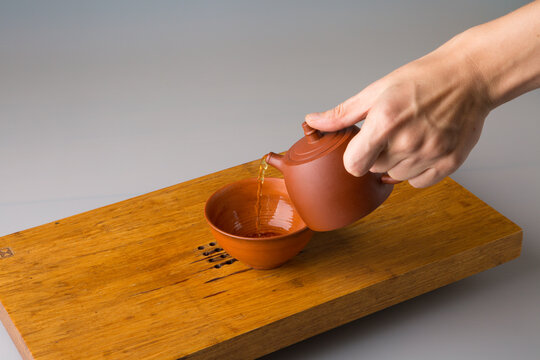 A man's hand pours freshly brewed pu erh tea from a clay teapot into a traditional cup. A cup on a table for tea ceremonies