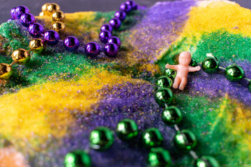 Closeup King cake with Mardi Gras beads and baby on vintage tray