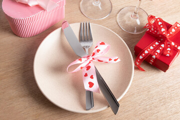 Cutlery and plate with red heart-shaped gift box on the table. Serving for a romantic dinner on valentines day concept.
