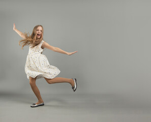 the concept of happiness, freedom, power, movement and people - a smiling young girl jumps in the air on a gray background