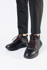 Stylish leather black short men's autumn sneakers on a white background on men's legs. Sneakers winter collection 2022.