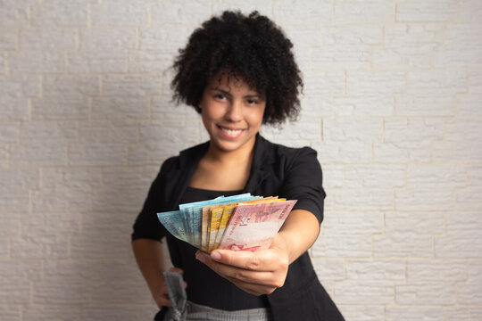 Black brazilian woman with curly hair displaying a spread of cash from Brazil. Business, income, loan, pay, buy, wealth concept.