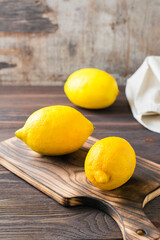 Whole ripe lemons on a wooden cutting board on the table. Organic nutrition, source of vitamins. Vertical view