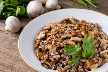 Buckwheat porridge with mushrooms in a white plate on wooden background