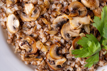 Buckwheat porridge with mushrooms in a white plate on wooden background
