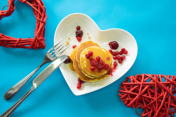Pancakes on a plate in the form of a heart, jam and berries, top view.
