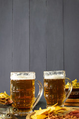 Mugs of cold beer with foam served on a wooden table with salty snacks in a wooden bowl
