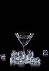 a martini glass surrounded by ice cubes on a black reflective background, with copy space