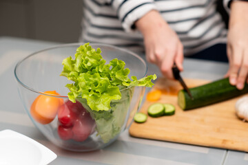 Fresh vegetables in a transparent plate on the table. Healthy eating. Nearby you can see the hands of a man who cuts a salad. The concept of healthy food. Health care.