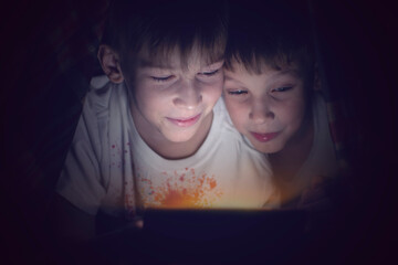 Two brothers are watching a movie or a cartoon under the covers on their gadget.