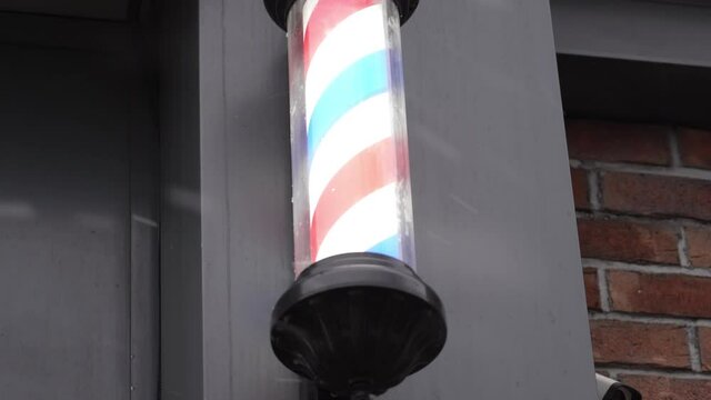 Red, white and blue barber pole on the side of the building with falling snow at winter. barbershop hairdresser traditional sign red blue and white spinning pole