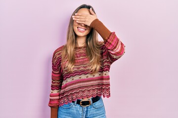 Beautiful hispanic woman wearing hippie sweater smiling and laughing with hand on face covering eyes for surprise. blind concept.