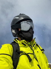 skier with yellow jacket, helmet, goggles and black face mask, under a light snowfall, with the...