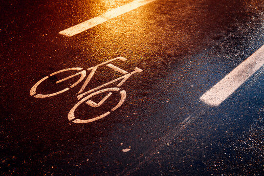 Symbol Fahrradweg bei Nacht auf nasser Fahrbahn. Regen und Straßenlichter