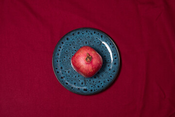 A blue dish with pomegranate on a red cloth.