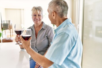 Senior caucasian couple smiling happy toasting with wine at the kitchen.