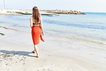 Fototapeta na wymiar Young cuacasian girl on back view wearing bikini walking at the beach.