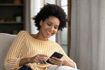 Smiling millennial African American relaxed woman entering payment information from credit card in...