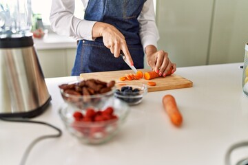 Obraz na płótnie Canvas Young blonde woman cutting carrot at kitchen