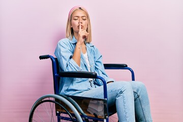 Beautiful blonde woman sitting on wheelchair asking to be quiet with finger on lips. silence and secret concept.