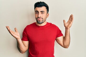 Young hispanic man wearing casual clothes clueless and confused with open arms, no idea and doubtful face.