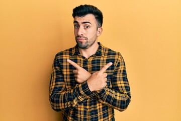 Young hispanic man wearing casual clothes pointing to both sides with fingers, different direction disagree