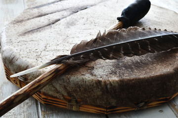 A close up image of a hand made leather meditation drum with sacred feather and drum stick. 
