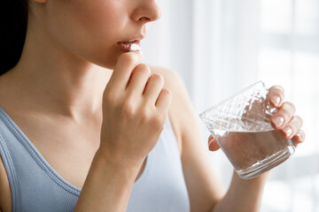 A young woman drinks medicine and holds a glass of water. - obrazy, fototapety, plakaty