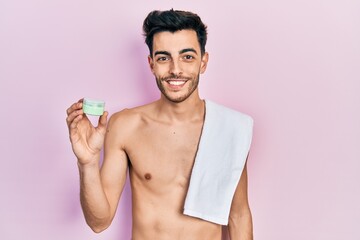 Young hispanic man shirtless wearing towel and eye bags patches looking positive and happy standing and smiling with a confident smile showing teeth