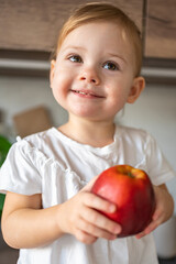 Baby girl blonde eating an apple in the kitchen, concept of healthy food for children