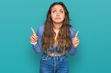 Young hispanic girl wearing casual clothes pointing up looking sad and upset, indicating direction with fingers, unhappy and depressed.
