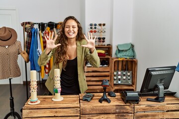 Beautiful hispanic woman working at fashion shop showing and pointing up with fingers number ten while smiling confident and happy.