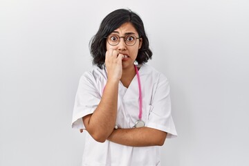 Young hispanic doctor woman wearing stethoscope over isolated background looking stressed and nervous with hands on mouth biting nails. anxiety problem.