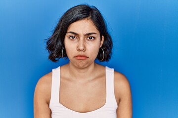 Young hispanic woman standing over blue background skeptic and nervous, frowning upset because of...