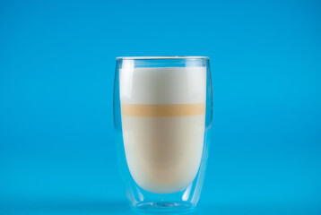 Yellow matcha latte of unripe mangoes on blue background. Matcha cocktail in double glass cup.