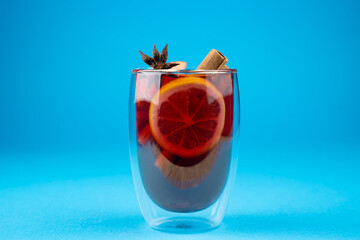 Mulled wine on blue background. Alcohol punch in double glass cup. Drink with orange, anise star,...