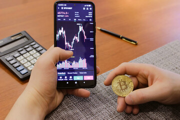 Physical bitcoin coin on the phone screen on the background of the Euro banknotes. Green arrow of the price growth chart