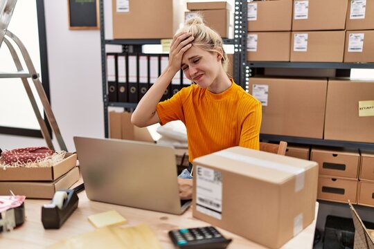 Young blonde woman working at small business ecommerce using laptop stressed and frustrated with hand on head, surprised and angry face